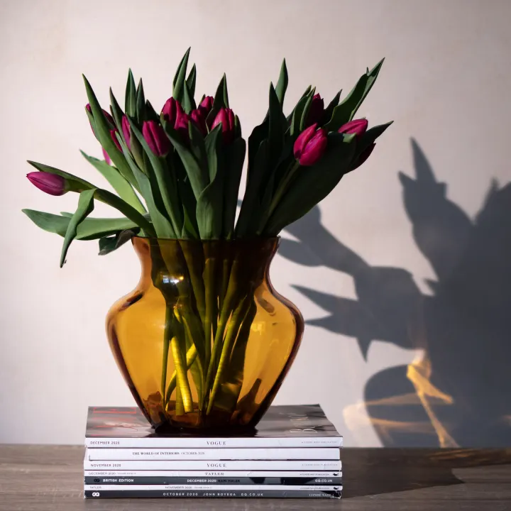 Jantarová váza Marika s červenými tulipány na stohu časopisů