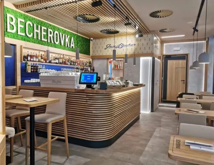 Bar Becherovka s dřevěným lamelovým obkladem a zeleným mechovým nápisem nad barovým pultem