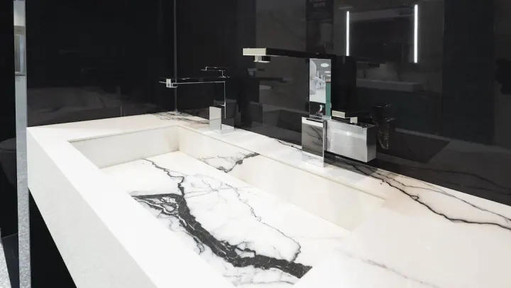Detail bílého umyvadla s černou mramorovou žílou, černá stěna a designová baterie