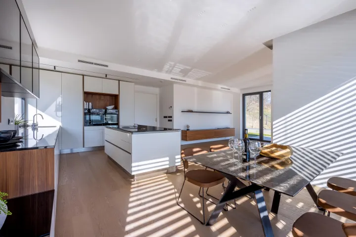 Bílá kuchyně s ořechovými prvky, ostrůvkem a jídelním stolem